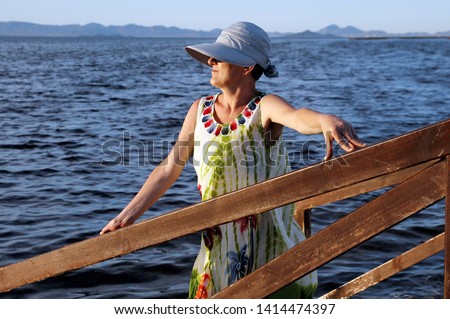 Mature woman, with hat playing with a handkerchief by the sea  in the wind by the sea at sunset, next to the salt flats  in the Mar Menor, Murcia, Spain, holidays, milf, holidays,