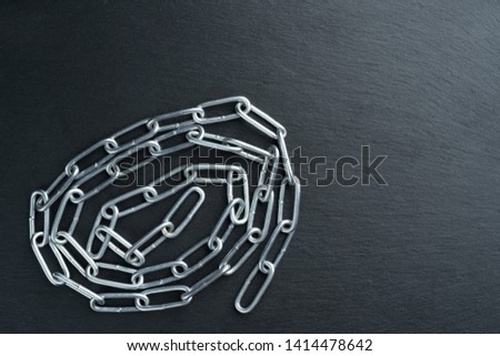 Convoluted shiny metal chain on a dark stone slate plate background. Copy space on the right.