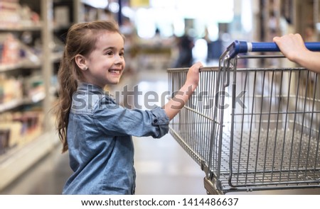 Mother and daughter in blue shirts shopping in supermarket using cart