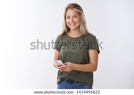 Indoor shot of pleasant good-looking positive woman receiving heartwarming video in app smiling delighted at camera holding smartphone checking messages posting pic in social network
