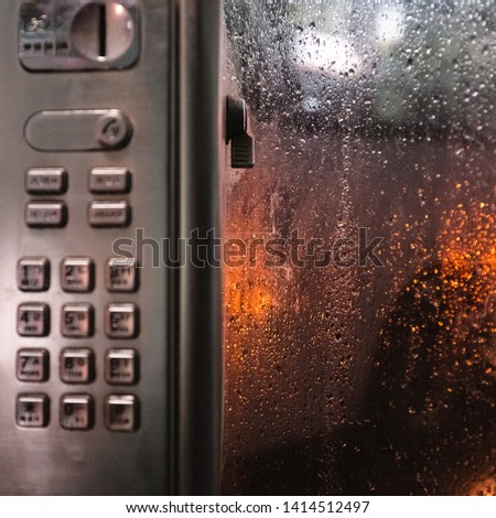 raindrops on the window on a rainy day, a bokeh of water droplets and traffic lights seen out of the window in phone booth, vertically picture