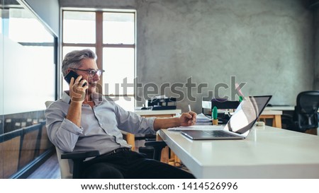 Businessman on the phone sitting at the laptop in his office. Male business professional in office talking on cell phone. Royalty-Free Stock Photo #1414526996