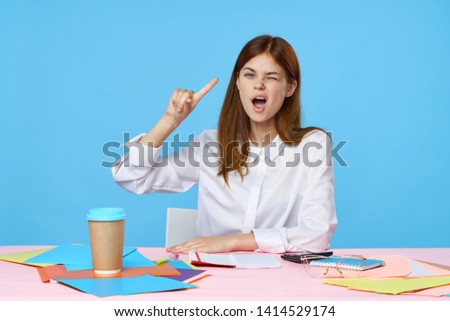 Business woman in a shirt sits at a table in the office and documents around                    