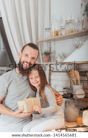 Single parent concept. Happy father and daughter together in kitchen, holding wrapped surprise gift, hugging, smiling.