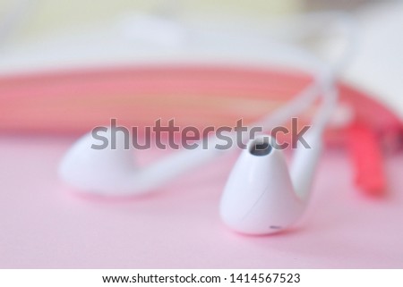 White headphones with a notebook, a book, an audiobook on a rose background. Blurry photo