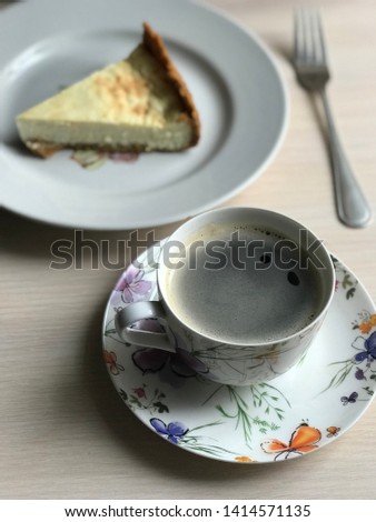 A cup of coffee, slice of cheesecake on the plate and fork on light wooden background. Beautiful delicious morning concept. Food blog recipe picture, sweets shop ad.