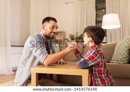 family, fatherhood and people concept - happy smiling father and little son arm wrestling at home in evening