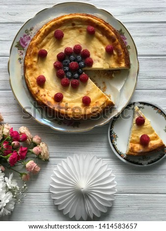 A cheesecake with blueberries and rasberries and bunch of flowers on light wooden background. Beautiful delicious morning concept. Food blog recipe picture, sweets shop ad.