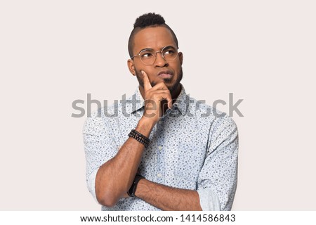 Thoughtful african guy thinking try solve problem pose isolated on grey studio background, worried black man in glasses feels concerned puzzled lost in thoughts pondering making decision concept image Royalty-Free Stock Photo #1414586843