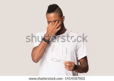 Young african american guy with closed eyes taking off glasses, massaging nose bridge, suffering from eye strain or dry eye syndrome, having rest, blurry eyesight, posing on grey studio background Royalty-Free Stock Photo #1414587002