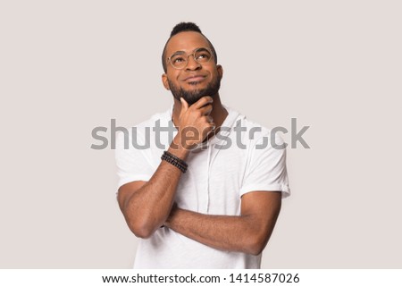 Black 30s guy in glasses touch beard daydreaming looks up posing isolated on grey studio background, mixed race man feels calm planning future, lost on positive thoughts, thinking and dreaming concept Royalty-Free Stock Photo #1414587026