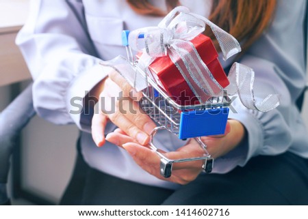 Red gift box in small shopping cart which on woman 's hands. 