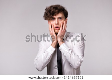 Portrait of young man with shocked emotional facial expression and hands gesture on light gray background