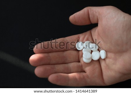 A hand with a handful of white pills on a black background, right side, copy space on a left, close up, selective focus