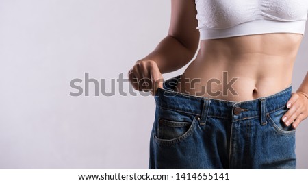 Young slim woman in oversized blue jeans. Fit woman wearing too large pants. Healthcare and woman diet lifestyle concept to reduce belly and shape up healthy stomach muscle. Royalty-Free Stock Photo #1414655141