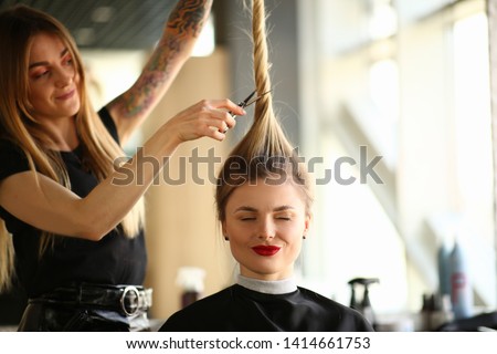 Tattooed Stylist Cutting Hair of Closed Eyes Woman. Hairdresser Using Scissors for Making Hairstyle for Female Client. Blonde Girl Getting Haircut in Beauty Salon. Hairstylist Styling New Hairdo