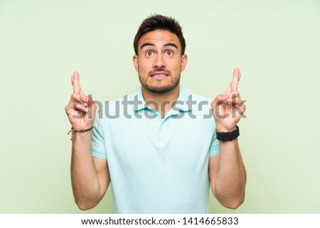 Handsome young man over isolated background with fingers crossing and wishing the best