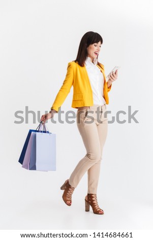 Image of a beautiful young business woman posing isolated over white background using mobile phone holding shopping bags.