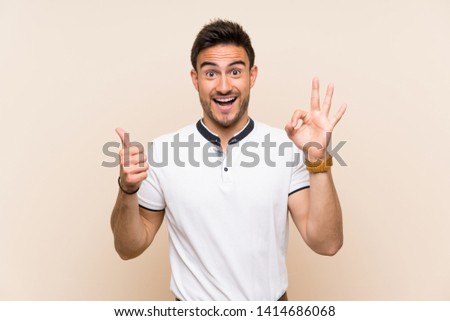 Handsome young man over isolated background showing ok sign and thumb up gesture