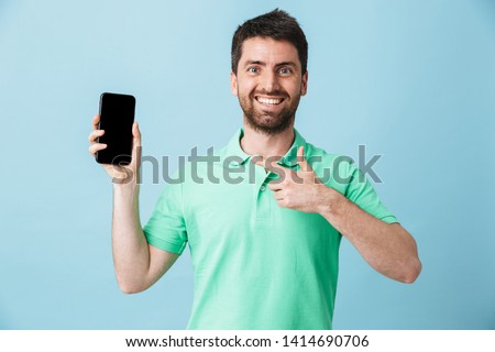 Portrait of a handsome bearded man wearing casual clothing standing isolated over blue background, showing blank screen mobile phone