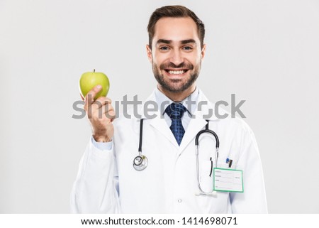 Portrait of professional young medical doctor working in hospital and holding green apple isolated over white background