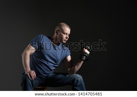 Young male dumbbell in his hands, shakes his muscles. Studio
