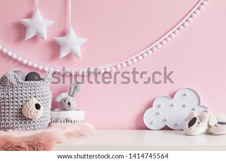 Cozy scandinavian newborn baby room with gray basket ,white stars lamp, cloud, plush rabbit and children accessories. Stylish interior with pink walls and haniging white garland.Template. Copy space. 