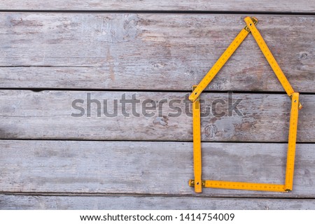 Meter rule folded in form of a house. House shape made from folding ruler on old wooden background. Space for text. Royalty-Free Stock Photo #1414754009