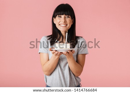 Image of a beautiful young woman posing isolated over pink wall background holding holiday birthday cake.