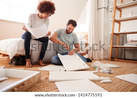 Couple In New Home Putting Together Self Assembly Furniture Royalty-Free Stock Photo #1414775591
