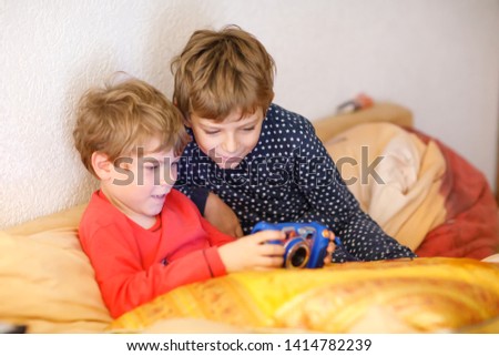 Two preschool or school kids boys, siblings and brothers having fun after school day playing video game at home and taking pictures with toy camera. Best friends, twins in pajamas or nightwear