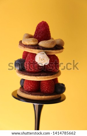 Raspberries, blueberries, cashew nuts and biscuits arranged as a cake on yellow background