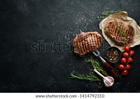 Grilled ribeye beef steak on the fork. At the aged table. Top view. Free space for your text. Royalty-Free Stock Photo #1414792310