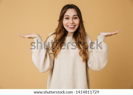 Beautiful young woman wearing sweater standing isolated over beige background, presenting copy space