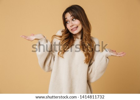 Beautiful young woman wearing sweater standing isolated over beige background, presenting copy space