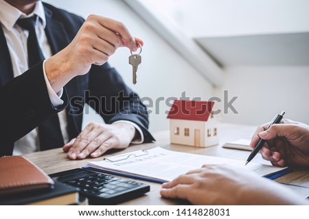 Estate agent giving house keys to client after signing agreement contract real estate with approved mortgage application form, concerning mortgage loan offer for and house insurance. Royalty-Free Stock Photo #1414828031