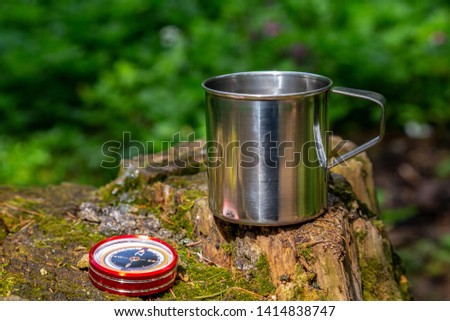 Tourist steel cup and compass in the summer forest