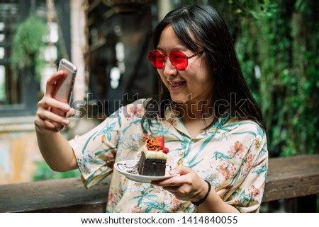 Young Fresh Asian girl wear red sunglasses and taking a photo with cake at vintage cafe..