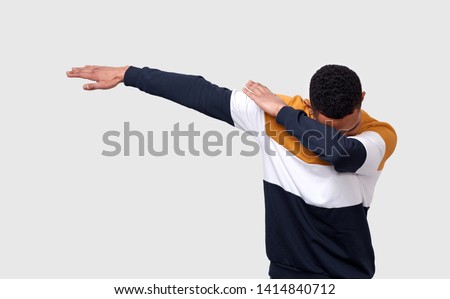 Studio shot of African American young man making dab pulling hands right tilting, covering his head with an arm, dancing and having fun over white background Royalty-Free Stock Photo #1414840712