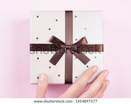 Woman's hand touching festive gift box with stars on pink background.