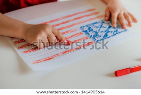 The child's hands paints the American flag on white table. Children's drawing of the flag of America. Independence day, July 4.