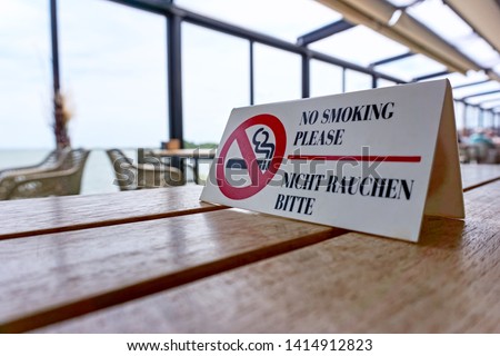 No smoking sign and text in English and German on a wooden table in a restaurant in the Netherlands                      