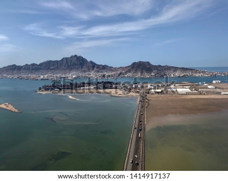 Middle eastern port city of Aden, beautiful mountain, blue sky and blue waters. Road with cargo trucks being loaded for much needed relief for Yemen Royalty-Free Stock Photo #1414917137