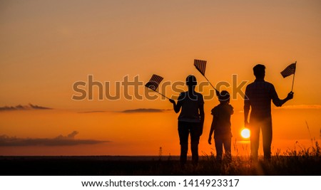 Family with child waving US flags at sunset, rear view
