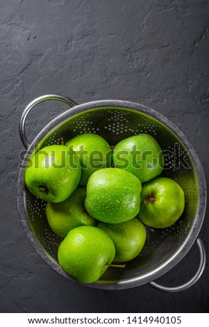 Fresh juicy green apple in stainless steel colander on Dark grey black slate background