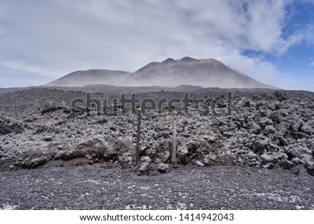 Landscape Picture of Mount Etna, active volcano in Sicily, Italy during cold and windy spring day. Black lava slope field under the top of volcano with main crater, Etna is highest volcano in Europe.
