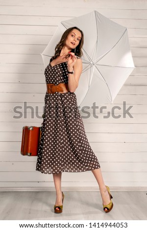 Girl in polka-dot dress with retro suitcase and umbrella. Mary Poppins style. Royalty-Free Stock Photo #1414944053