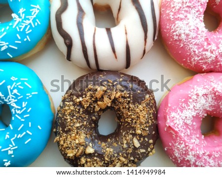 Picture of assorted donuts with chocolate frosted, vanile glazed, blue glazed and pink glazed and sprinkles donuts. Close up. Backgound texture.