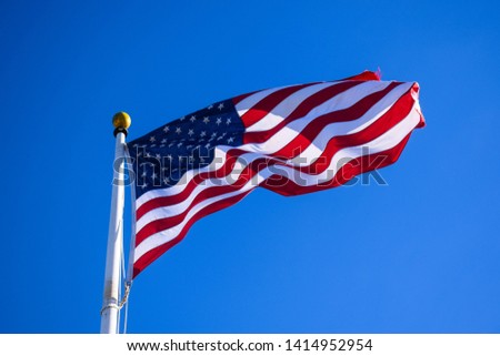 Close-up photo of the United States of America flag blowing in the wind on a clear blue sky.