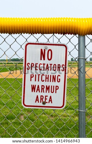 No spectator pitching warmup area sign on fence with baseball/ softball field in the background.